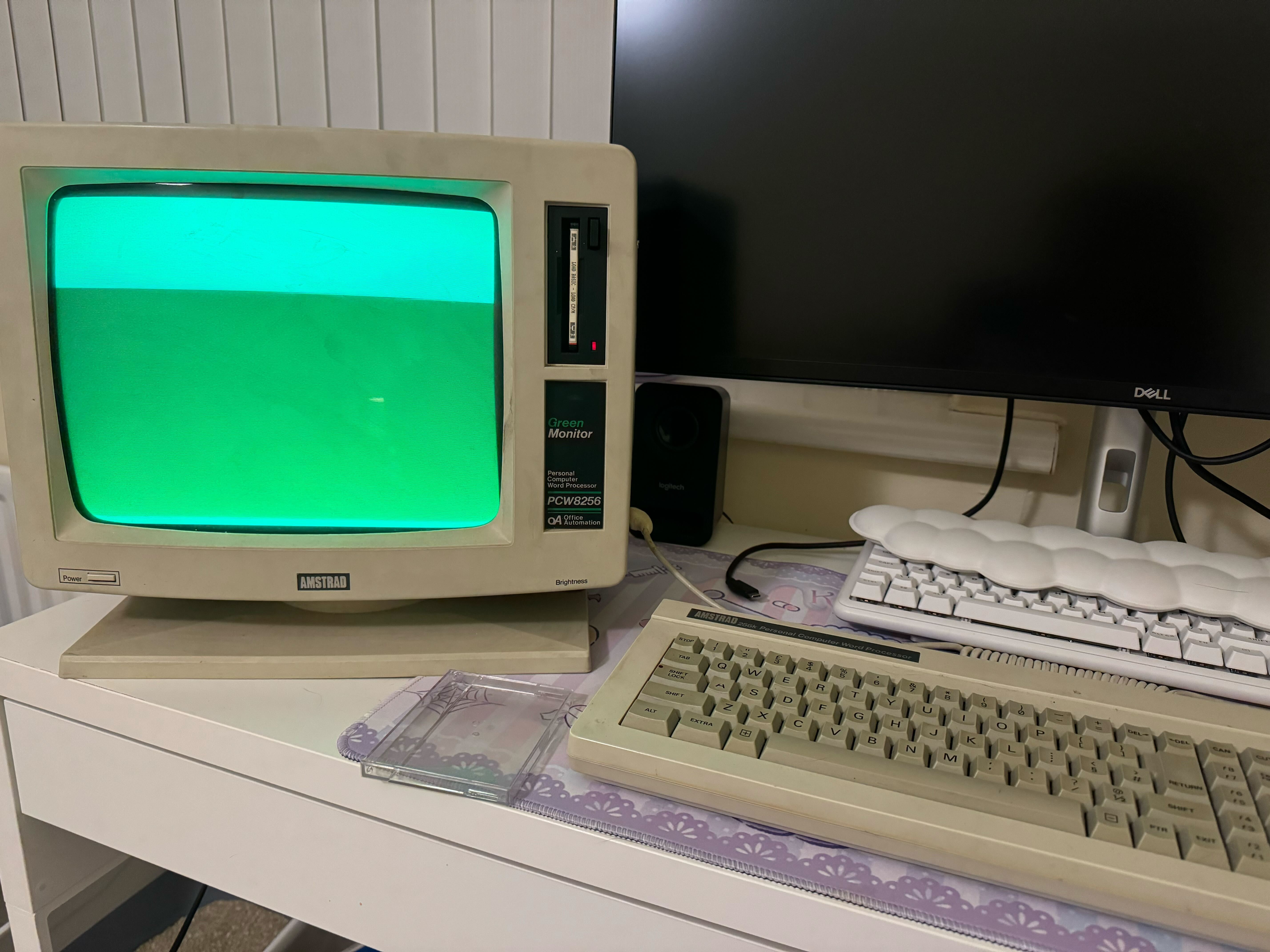 An Amstrad PCW 8256 monitor next to its keyboard, powered on with a blank, green screen.